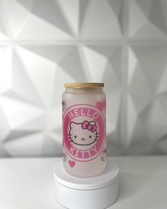 a pink hello kitty jar sitting on top of a white stand next to a wall