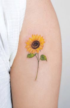 a small sunflower tattoo on the right arm and shoulder, with green leaves around it