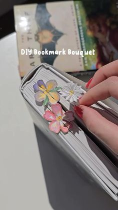 a woman's hand is holding onto a book with flowers on it and the title diy bookmark bouquet