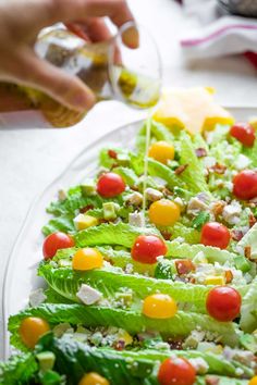 a salad with lettuce, tomatoes and cheese being drizzled onto it