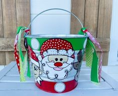 a bucket with a santa clause painted on the side and ribbon hanging from it's handle