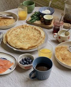 a table topped with plates and bowls filled with breakfast foods next to cups, saucers and utensils