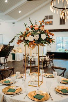 an elegant centerpiece with orange and white flowers sits on a gold plated table