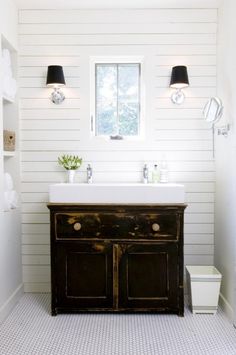 a bathroom with white walls and black cabinet in the center, two lights on either side of the sink