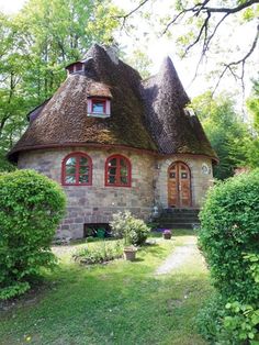 an old stone house with a thatched roof and red trimming on the windows