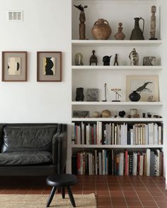 a black leather couch sitting in front of a book shelf filled with books and vases