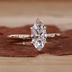 an oval cut diamond engagement ring on top of a wooden surface with leaves around it