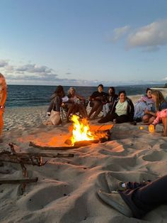 a group of people sitting around a campfire on the beach