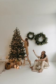 a man and woman sitting next to a christmas tree