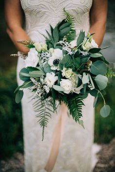 a bride holding a bouquet of flowers and greenery