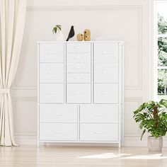 a white cabinet with many drawers in a room next to a potted plant and window