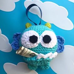 a crocheted stuffed animal with big eyes holding a roll of money in it's mouth