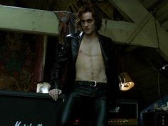 a shirtless man with no shirt standing in front of a guitar case and wearing black leather pants