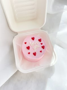 a small pink cake with hearts on it in a plastic container that says i love you