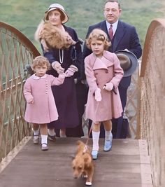 three people and two children are standing on a bridge with a dog in the foreground