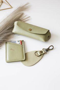 two leather keychains and a card holder on a white surface with feathers in the background