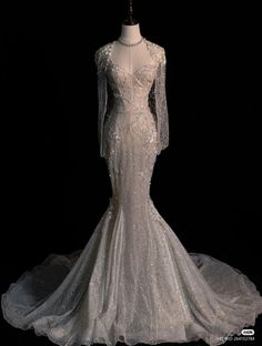 a white wedding dress with long sleeves and sheer lace on the skirt is displayed in front of a black background