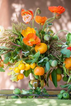 a vase filled with oranges and flowers on top of a table