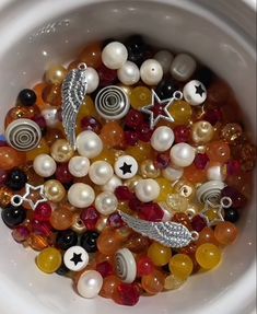 a white bowl filled with lots of different types of beads and brooches on top of each other