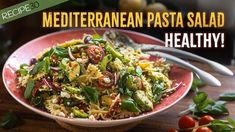 a bowl filled with pasta and vegetables on top of a wooden table next to tomatoes