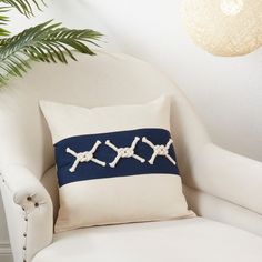 a white chair with a blue and white pillow on top of it next to a potted plant