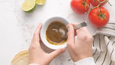 a person holding a cup of coffee next to tomatoes and limes