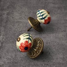 two decorative knobs with red and blue flowers on them sitting on a gray surface