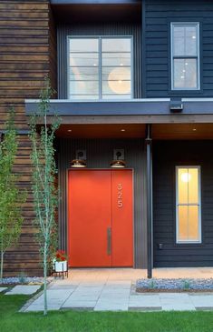 two red doors are in front of a black house with wood sidings and green grass