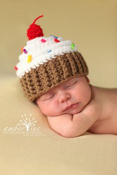 a newborn baby wearing a knitted hat with a cherry on top and white frosting