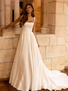 a woman in a white wedding dress leaning against a stone wall with her arms outstretched