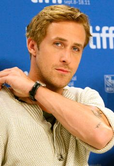 a man with a watch on his left hand and wristband around his neck, standing in front of a blue backdrop