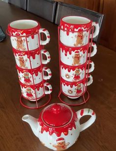 a set of four christmas themed teapots and saucers on a wooden table