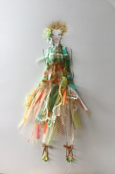 a woman's dress made out of different colored ribbons and fabric strips, hanging on a wall