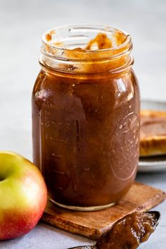 an apple and spoon sitting next to a jar of peanut butter