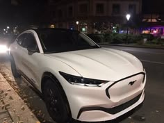 a white car is parked on the side of the road at night with two cars behind it