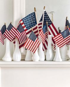 several american flags are placed in white vases on a mantle with candlesticks