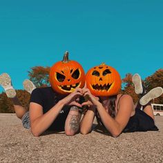 two people laying on the ground with pumpkins in front of their faces and hands