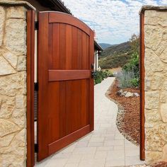 an open wooden door leading to a stone building with a path between it and another house in the background