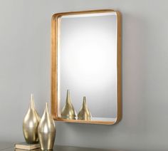 a mirror sitting on top of a wooden table next to vases and a book