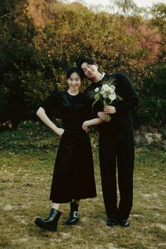 a man and woman standing next to each other in front of some bushes with flowers