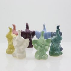 small ceramic elephant figurines are lined up on a white surface, each with different colors