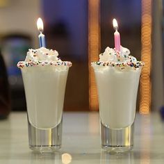 two glasses filled with white frosting and sprinkles, one has a lit candle in it