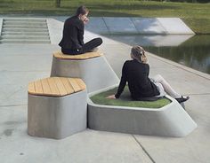 two people are sitting on concrete benches near the water and grass in front of them