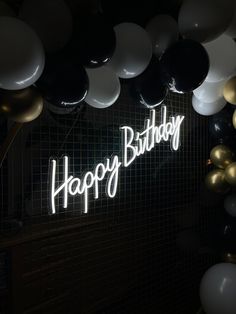 a birthday party with balloons and the words happy birthday lit up in white on a black wall