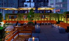 an outdoor seating area with tables and umbrellas on the roof terrace at night time