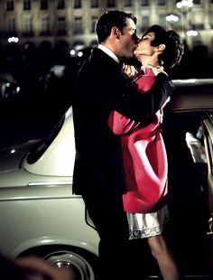 a man and woman kissing in front of a car