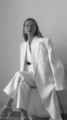 a woman sitting on top of a chair wearing a white suit and high heel shoes