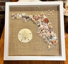 a sea shell map is displayed in a white frame on a table next to other seashells