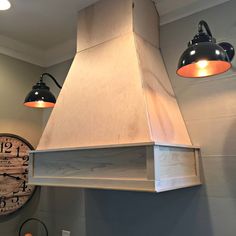 two lamps are hanging from the ceiling above a stove top hood in a kitchen with a clock on the wall behind it