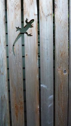 a metal lizard sitting on top of a wooden fence